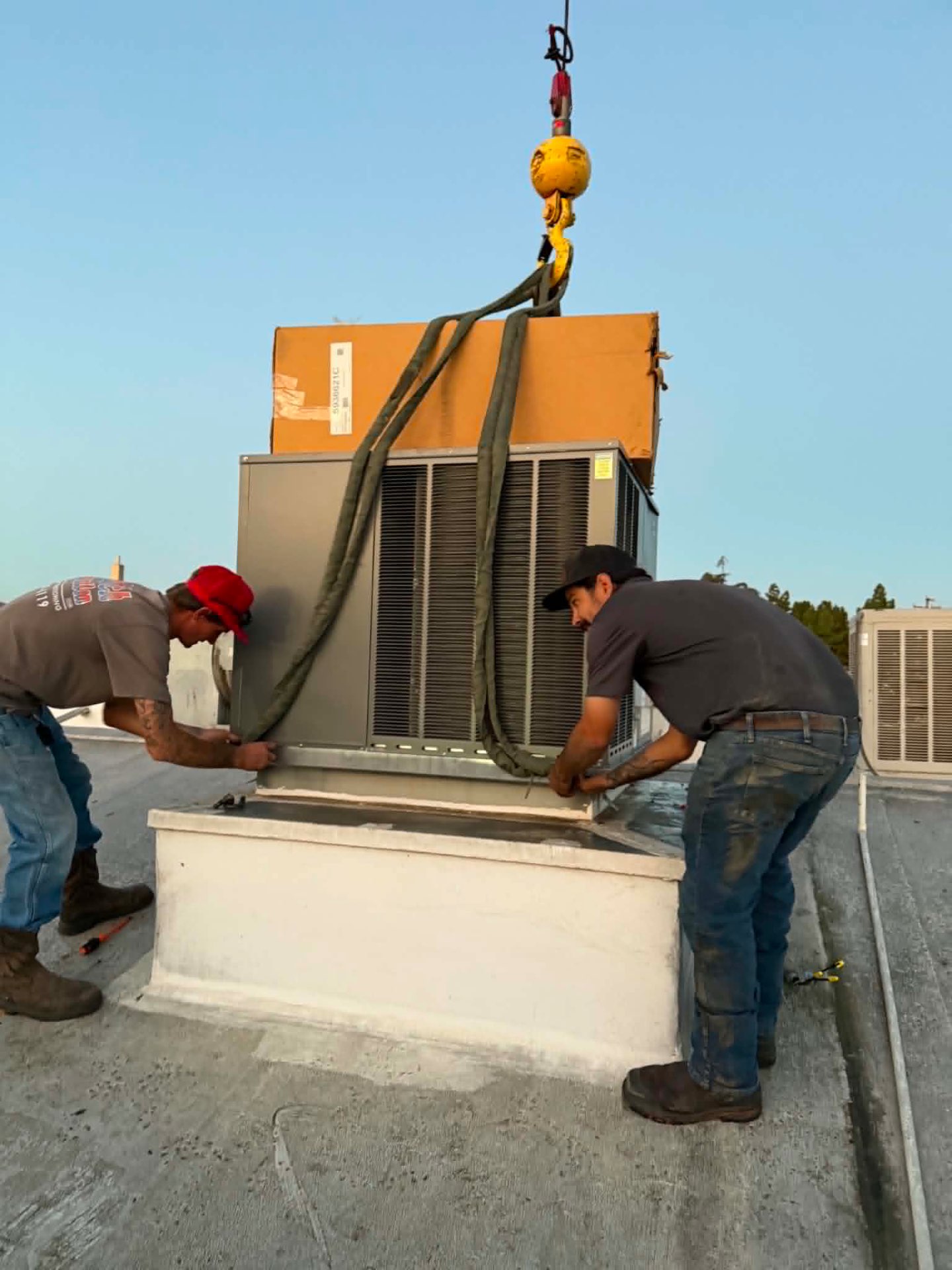 ColdTech technicians guiding a boxed commercial HVAC unit lowered by crane onto a rooftop curb