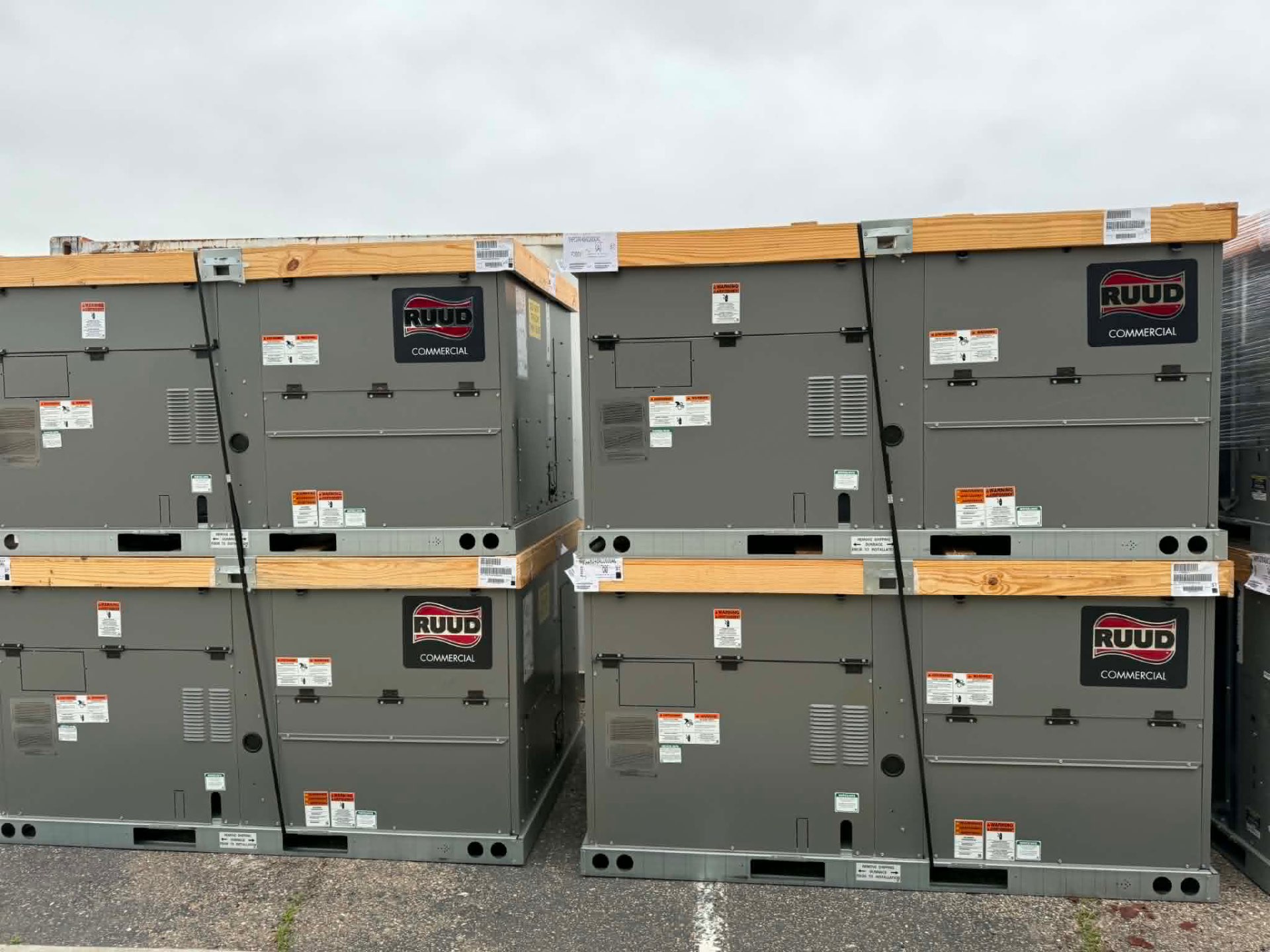 Stacked pallet of new crated RUUD Commercial rooftop package units staged outdoors before a 805-area commercial installation