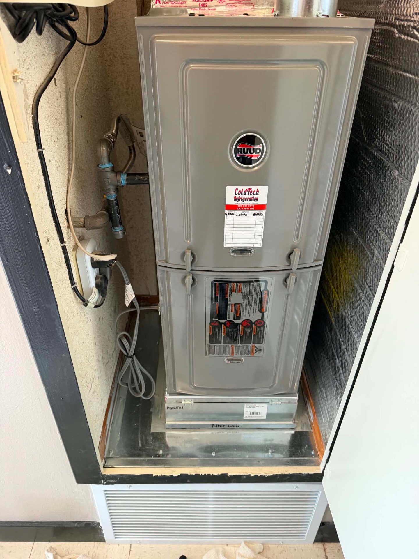 RUUD residential gas furnace freshly installed in an indoor utility closet with a red-and-white ColdTech Refrigeration service sticker on the front panel