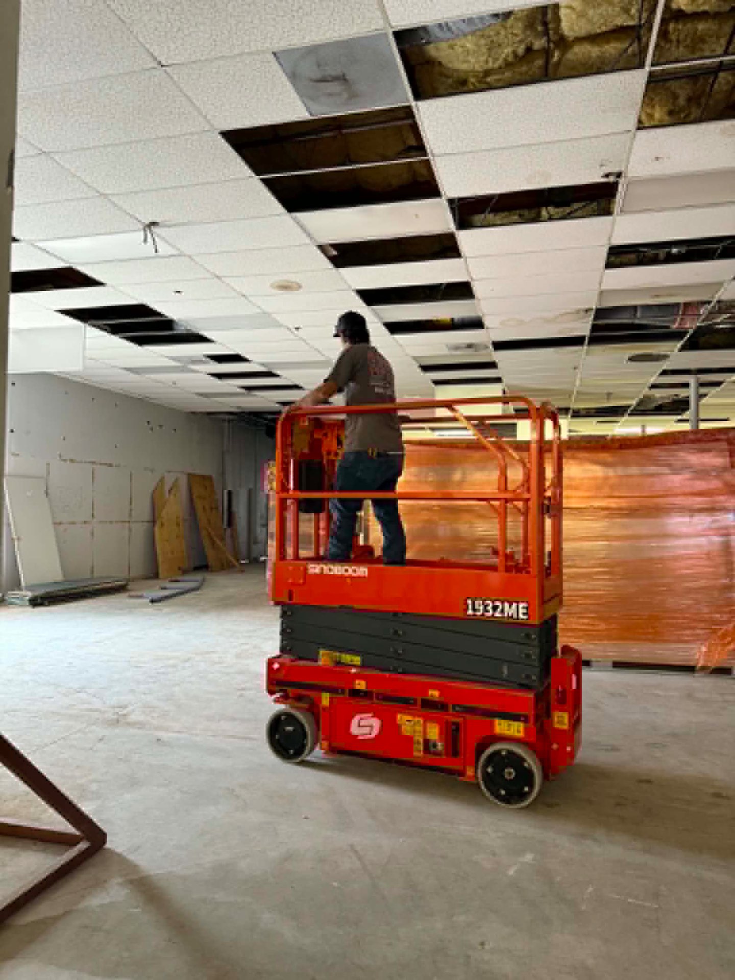 ColdTech technician on an orange scissor lift removing ceiling tiles inside a commercial tenant space during an HVAC and ductwork installation