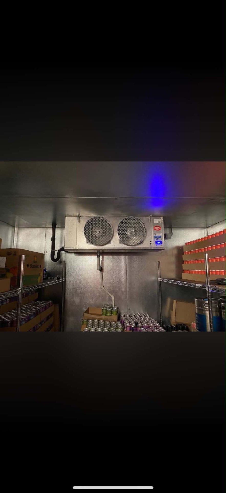 Interior of a commercial walk-in cooler storing kegs and canned beverages with a Heatcraft evaporator on the ceiling