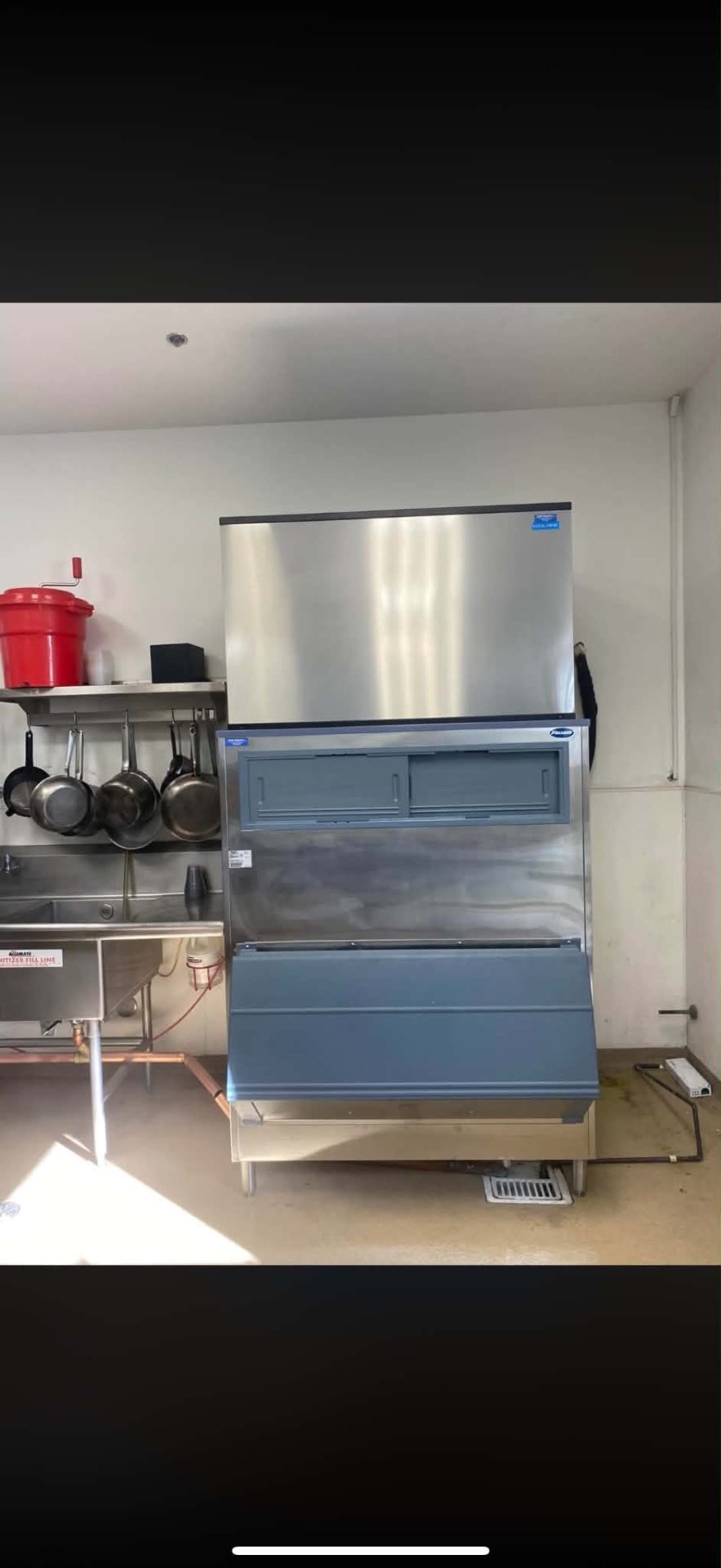 Large stainless-steel commercial ice machine and storage bin installed in a restaurant kitchen
